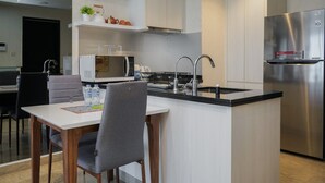 A modern kitchen with a central island, stainless steel appliances, and a dining area with a table and chairs. - Minimalist And Cozy 1Br At Branz Bsd City Apartment (Pagedangan)