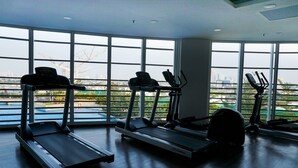 A gym with treadmills and elliptical machines, large windows, and a view of a cityscape. - Nice And Comfy Studio West Vista Apartment (Jakarta)