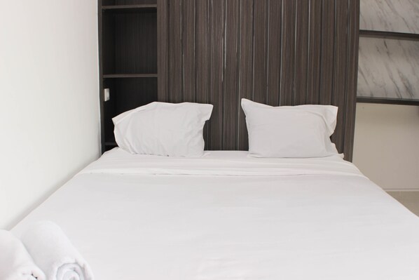 A neatly made bed with white linens and pillows, a wooden wardrobe, and a marble wall.