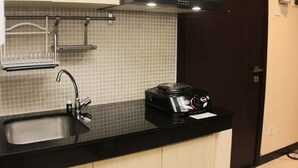 A kitchen with a black countertop, a sink, a stove, and a tiled backsplash. - Comfort 1Br At Sky Terrace Apartment (Jakarta)