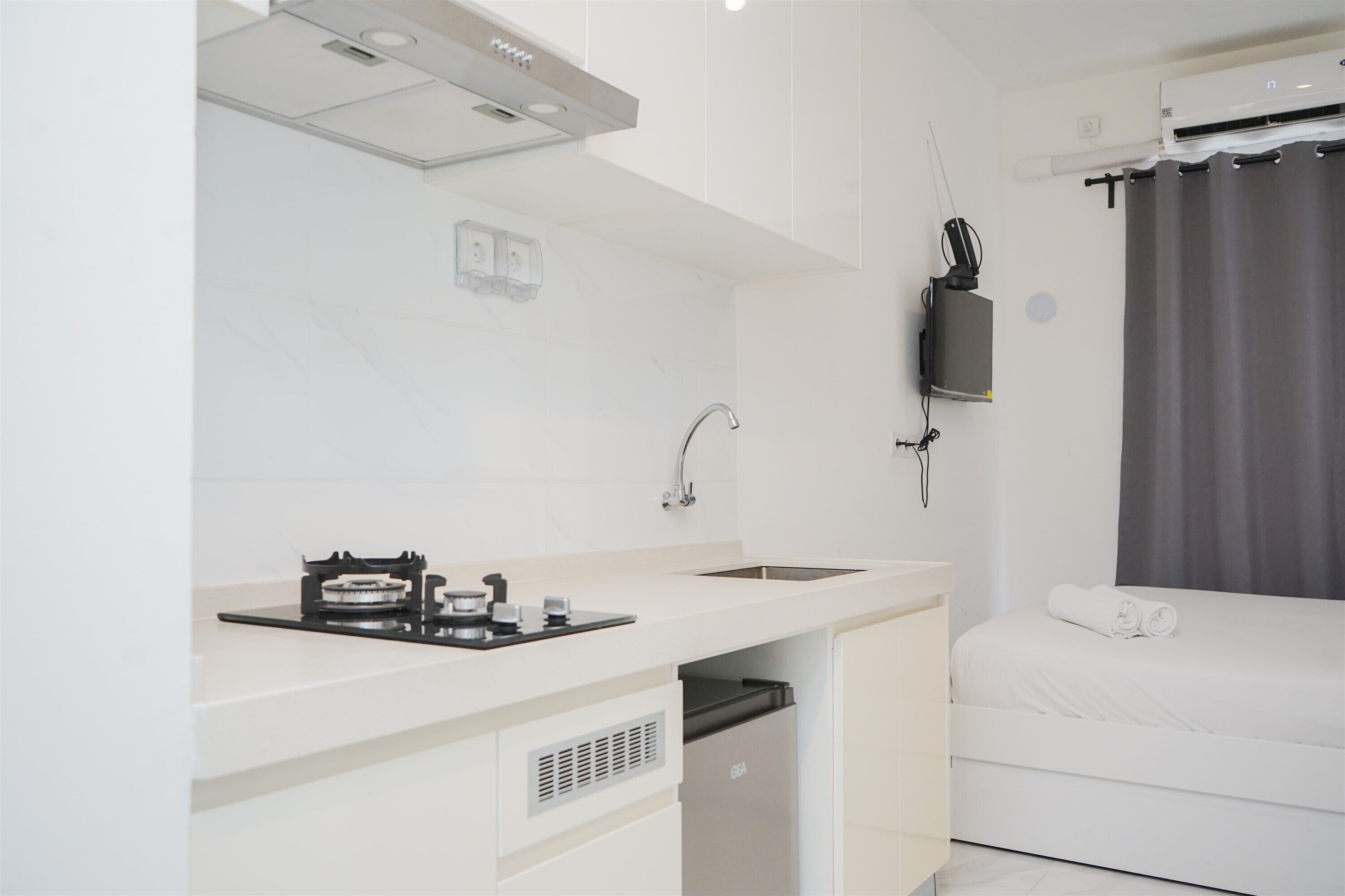 A compact hotel room with a kitchenette, a bed, and a window with curtains.