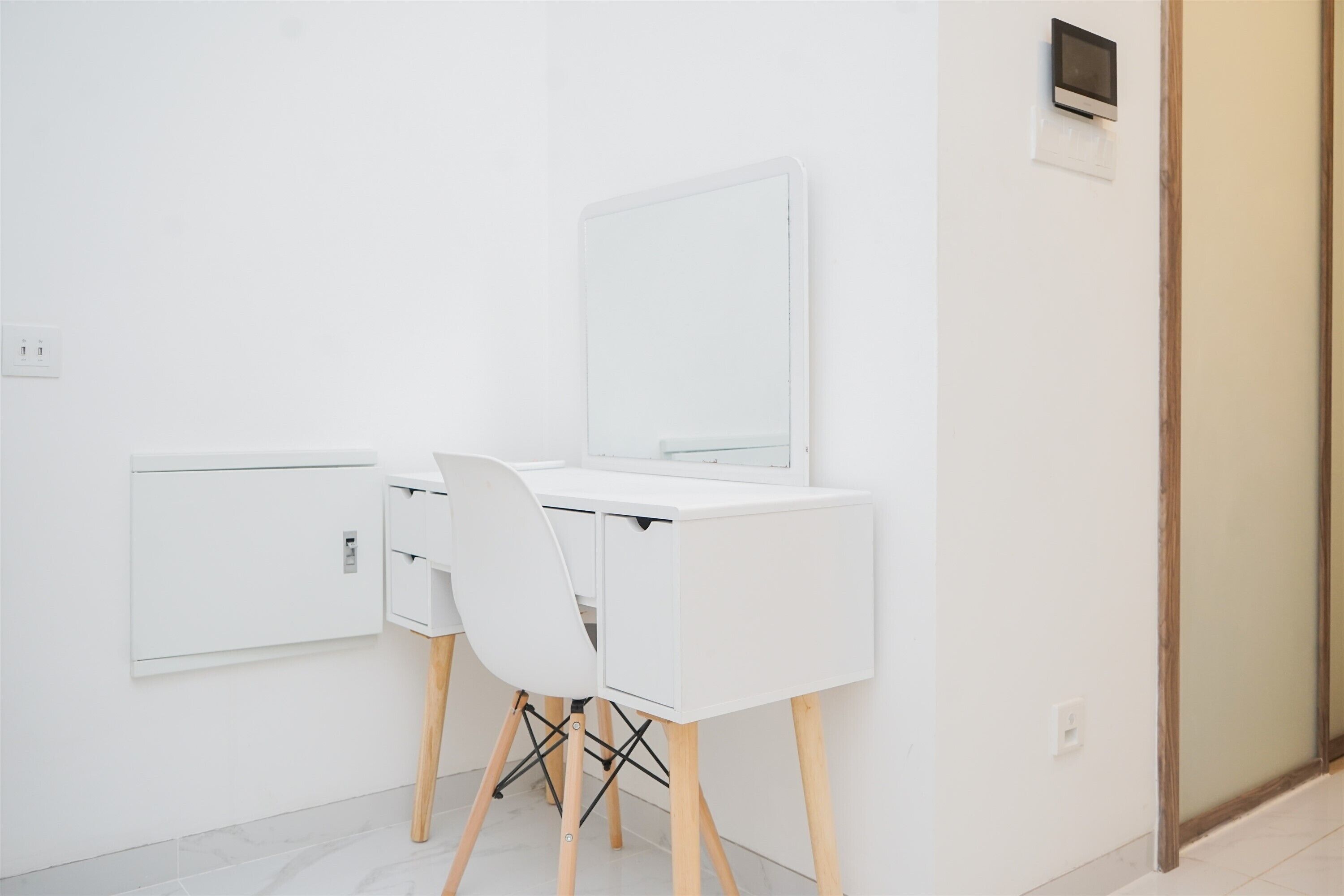 Un escritorio blanco con un espejo y una silla, un interruptor de luz y un termostato en la pared.