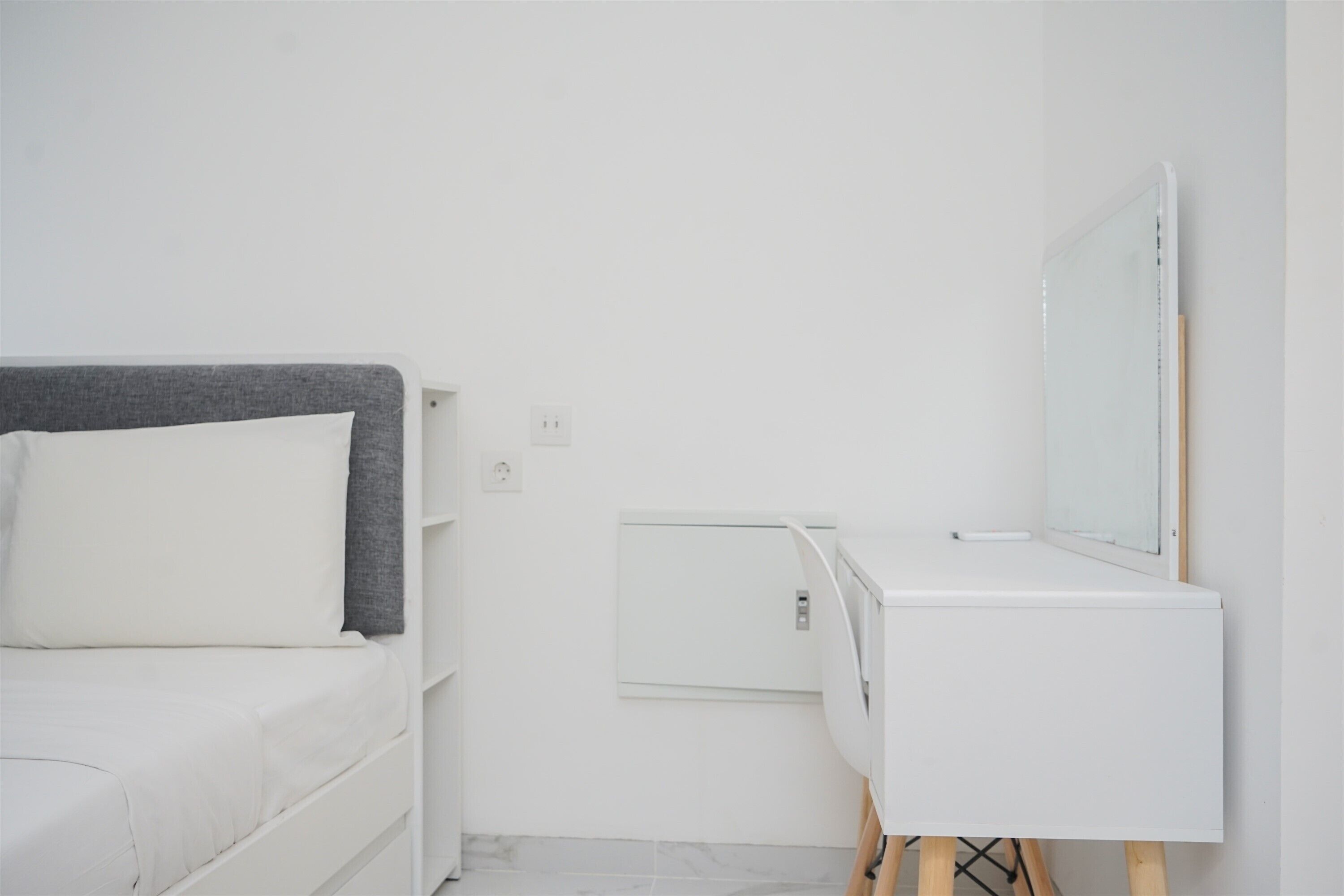 A minimalist room with a bed, a small white dresser, and a mirror.