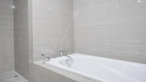 Een moderne badkamer met een vrijstaand bad, betegelde wanden en een douchegedeelte.