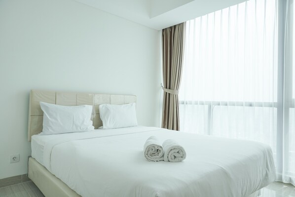 Una habitación de hotel con una cama grande, ropa de cama blanca y un ventanal con cortinas.