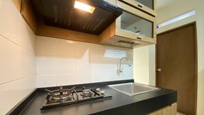A kitchen with a gas stove, a sink, and wooden cabinets. - Cozy 3Br Furnished Apartment At Gateway Ahmad Yani Cicadas (Bandung)