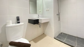 A bathroom with a toilet, sink, mirror, and shower. - Cozy Studio Apartment At Beverly Dago (Bandung)