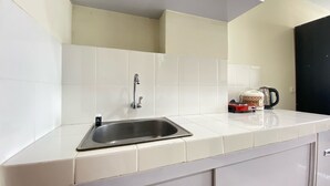 A kitchen with white tiles, a stainless steel sink, and a kettle on the counter. - Cozy Studio Apartment At Beverly Dago (Bandung)