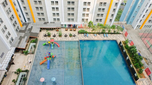 A rooftop pool area with a slide and a separate swimming pool, surrounded by a multi-story building with balconies. - Nice And Cozy Studio At Paramount Skyline Serpong Apartment (Gading Serpong)