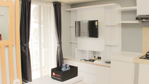 Een moderne hotelkamer met een flatscreen televisie aan een witte muur, een zwarte opbergkist met waterflessen, en een raam met zwarte gordijnen.