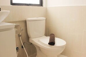 Un inodoro con una toalla encima, una tubería visible y una ventana sobre el inodoro.