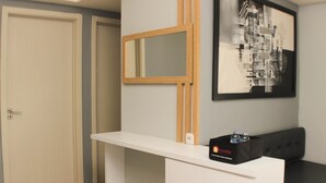 Een kamer met een wit receptiebalie, een zwart-wit abstract schilderij aan de muur, een deur en een zwarte tas op het bureau.