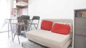 A compact living space with a sofa bed, a dining area with chairs, a kitchen area with a stove, and a cabinet. - Best Deal And Comfy 2Br At Green Pramuka City Apartment (Jakarta)