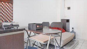 A compact kitchenette with a Rinnai stove, a travel food box, a small table, and a sofa with a red pillow. - Best Deal And Comfy 2Br At Green Pramuka City Apartment (Jakarta)