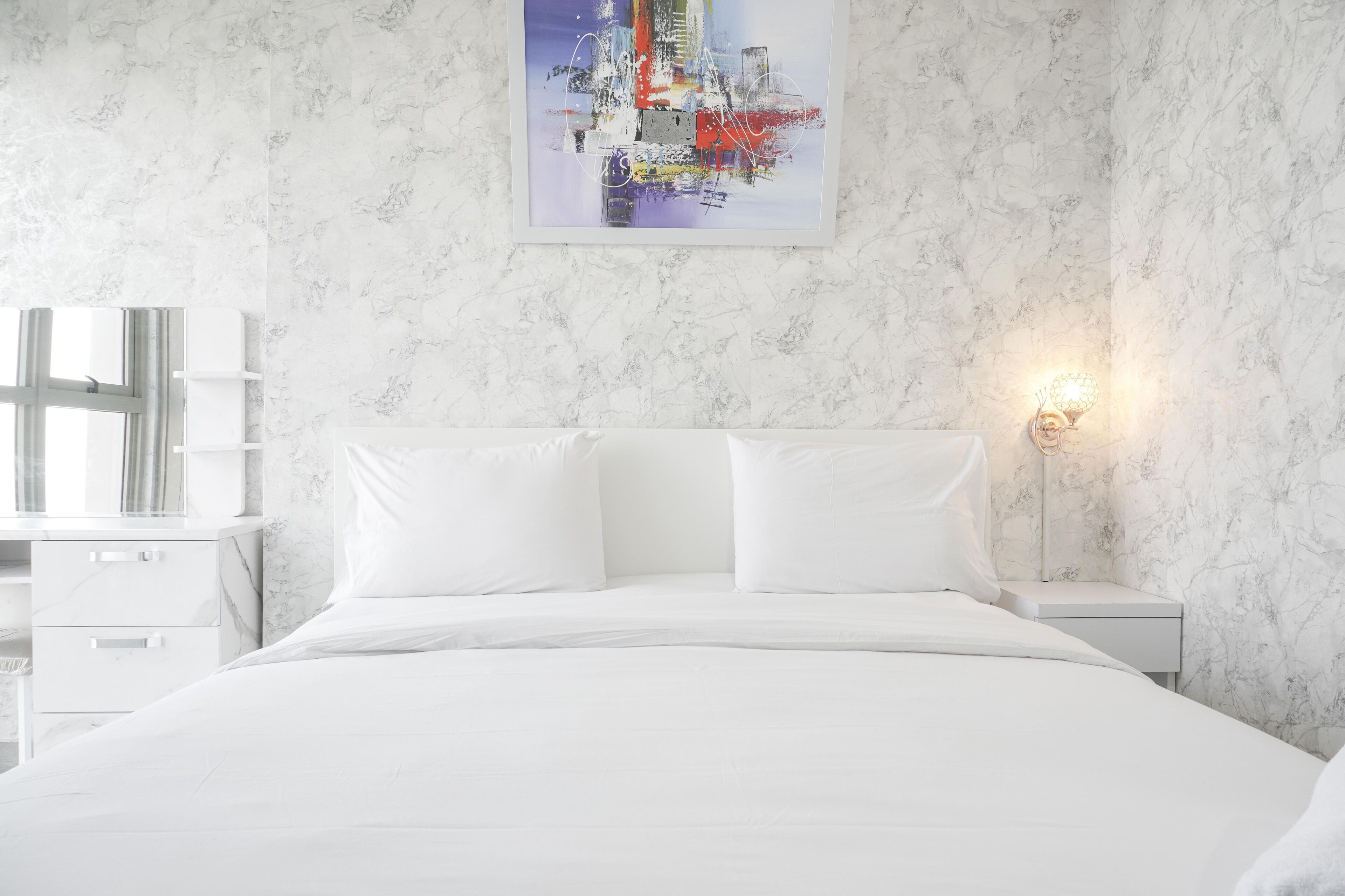 Une chambre à coucher avec un lit, des tables de chevet blanches, un tableau accroché au mur et une fenêtre.