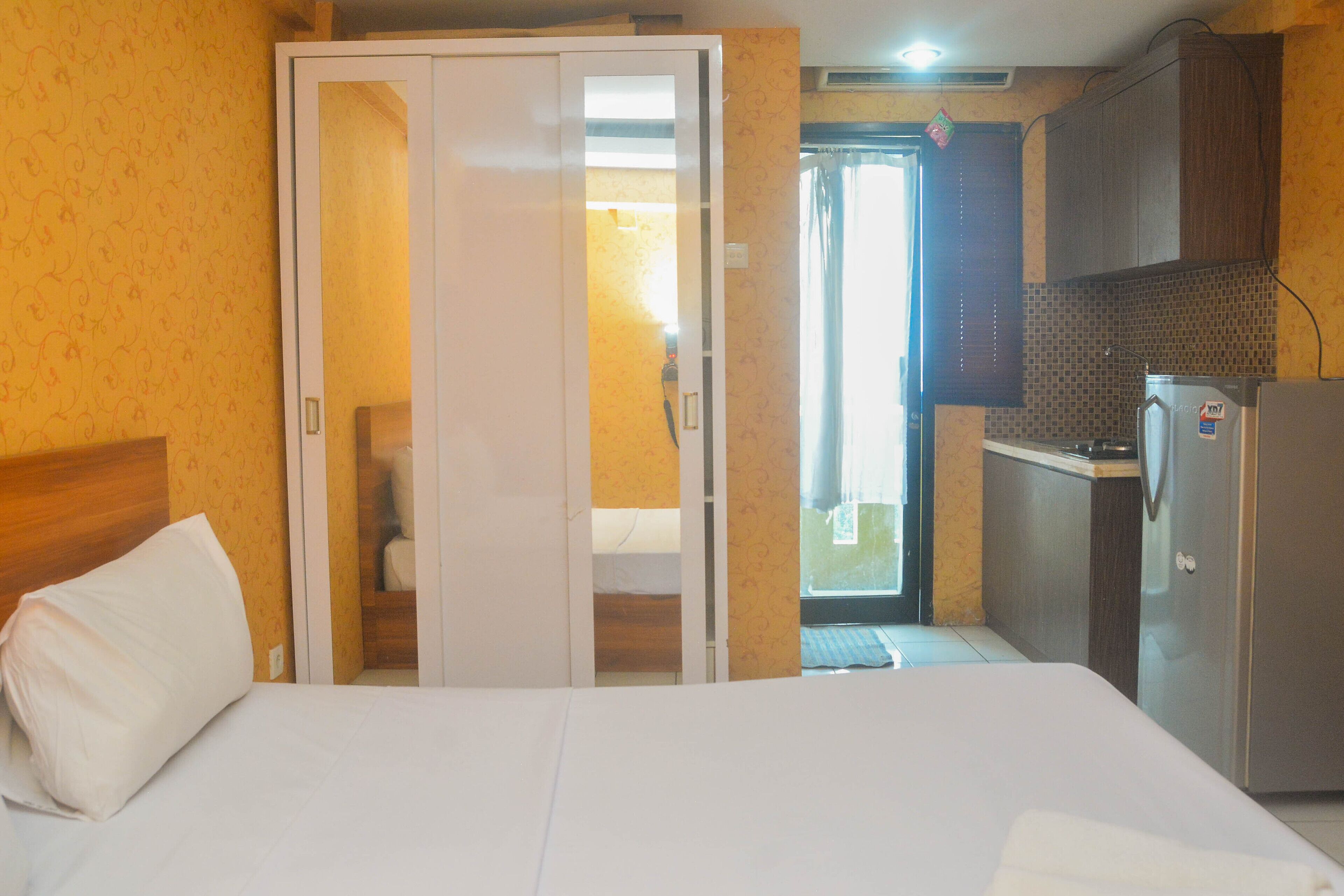 Quarto de hotel com cama, guarda-roupa, kitchenette e casa de banho visível através de uma porta aberta.