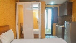 A hotel room with a bed, a wardrobe, a kitchenette, and a bathroom visible through an open door. - Cozy Studio At Kebagusan City Apartment (Jakarta)