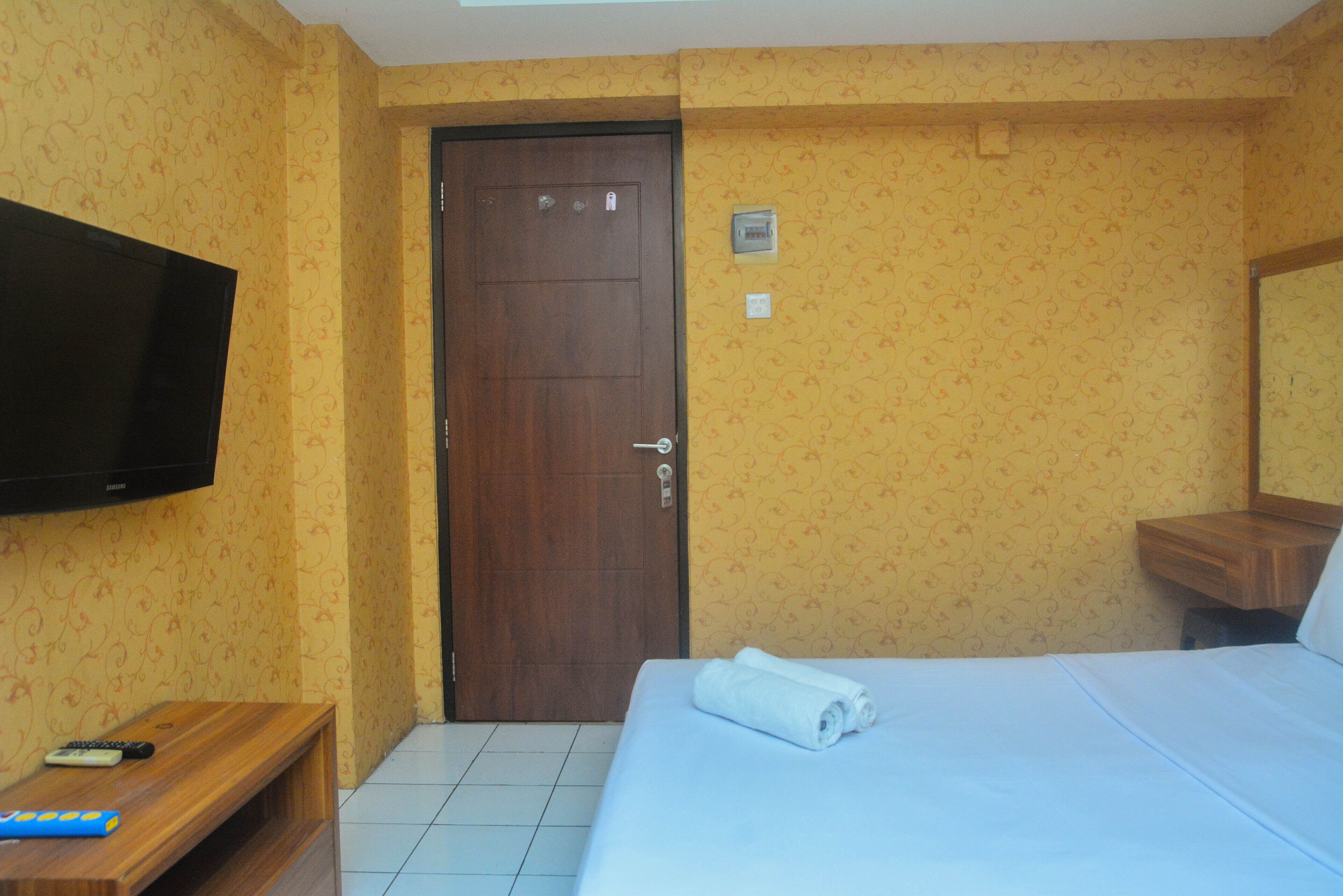 Ein Hotelzimmer mit einem Bett, einem an der Wand befestigten Fernseher, einer hölzernen Bank und einer Tür.