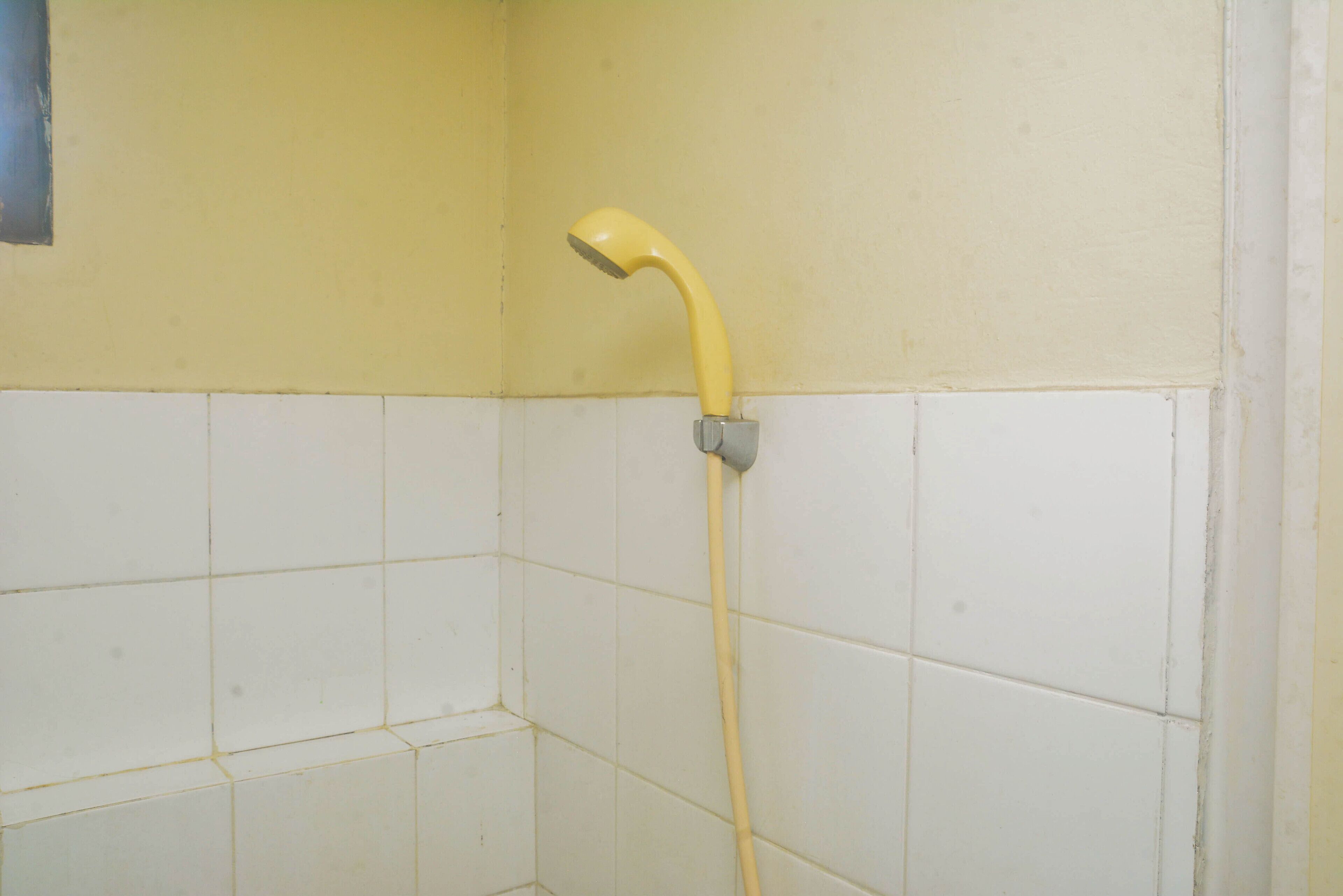 A yellow showerhead mounted on a white tiled wall in a bathroom.