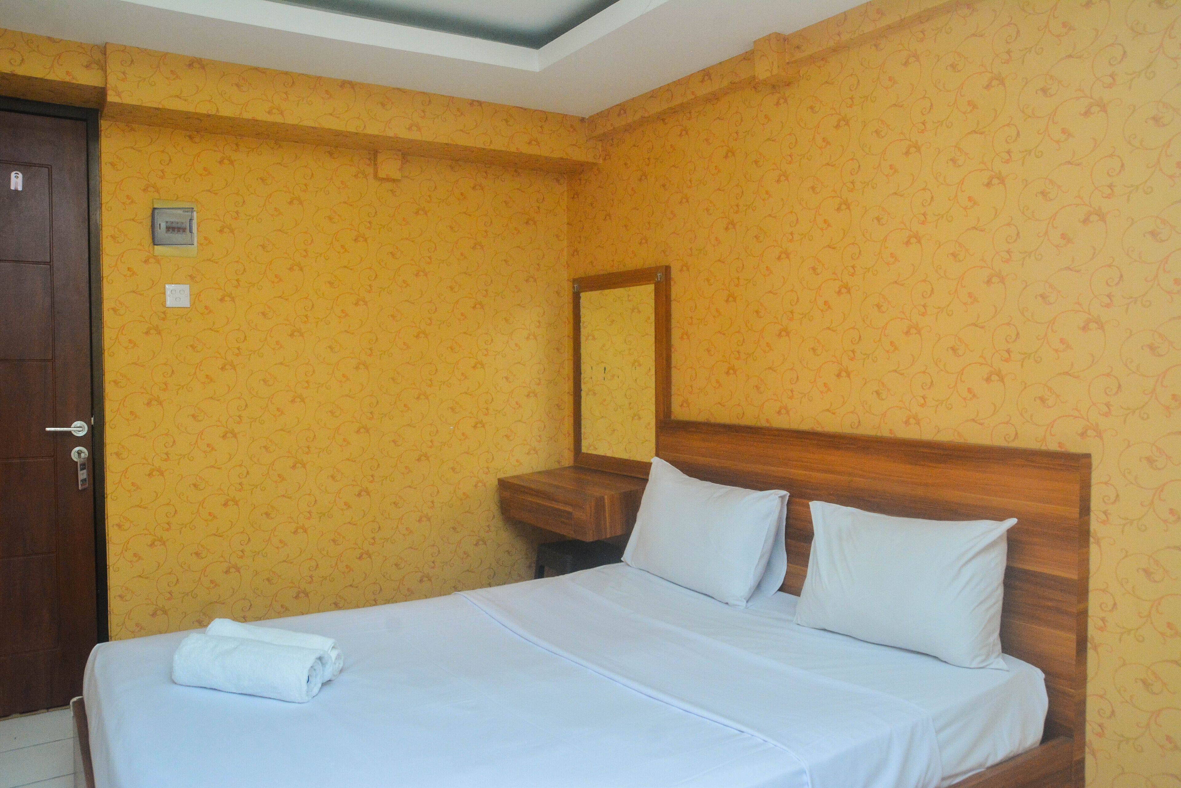 A hotel room with a bed, a wooden nightstand, a mirror, and a door.