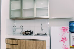 Modern kitchen with a stainless steel sink, utensil basket, compact electric cooker, and white refrigerator.