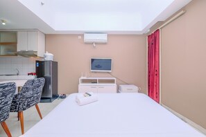 A hotel room with a bed, a desk, a chair, a TV, a minibar, and a window.