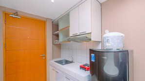 A compact kitchen with a sink, a refrigerator, and a wooden door. - Warm And Cozy Stay Studio Apartment Margonda Residence 2 (Depok)