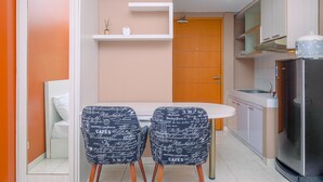 A compact kitchen with a white table, two chairs with a cafe-themed pattern, a built-in oven, and a wooden door. - Warm And Cozy Stay Studio Apartment Margonda Residence 2 (Depok)