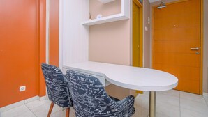 A dining area with a white table and two chairs with a black pattern. There is a white shelf above the table and a wooden door in the background. - Warm And Cozy Stay Studio Apartment Margonda Residence 2 (Depok)