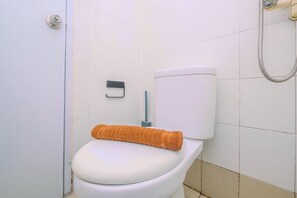 A toilet with a towel on the seat, a toilet paper holder, and a shower hose.