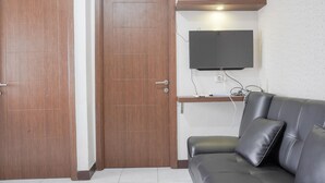 A room with a wooden door, a black leather sofa, and a mounted flat-screen TV. - Nice And Cozy 2Br At Cinere Resort Apartment (Depok)