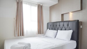 A neatly made bed with white linens and a rolled towel, a tufted headboard, and a window with curtains. - Nice And Cozy 2Br At Cinere Resort Apartment (Depok)