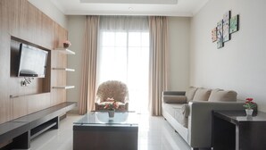 A modern living room with a flat-screen TV, a glass coffee table, a sofa, and a chair. - Cozy Stay And Tidy 1Br At The Bellezza Apartment (Jakarta)