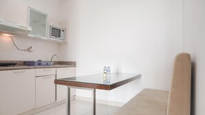 A modern kitchen with white cabinets, a microwave, and a glass-top table with two bottles. - Cozy Stay And Tidy 1Br At The Bellezza Apartment (Jakarta)