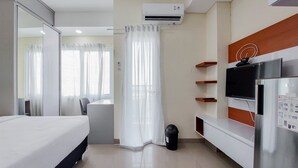 Quarto de hotel com cama, escrivaninha, televisão e frigorífico.
