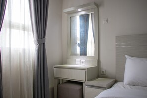 A hotel room with a bed, a bedside table, a mirror, and a window with curtains. - Minimalist 1Br Apartment With Pool View At Atlanta Residences (Depok)