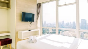 Quarto de hotel com uma cama grande, uma televisão fixada na parede, uma janela com vista para a cidade e uma pequena mesa de trabalho com uma cadeira.