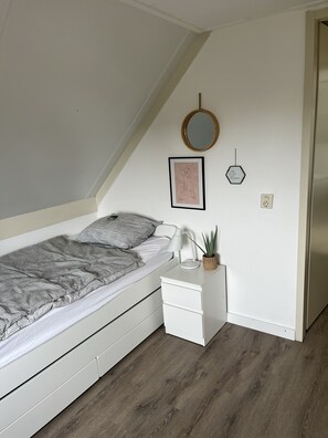 Cozy bedroom with a single bed, bedside table, and a sloped ceiling.