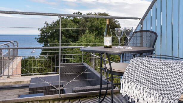 Un balcon avec une table, deux chaises, une bouteille de vin et un verre.