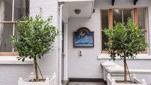 Un bâtiment blanc avec deux arbres en pot devant, une porte et une enseigne représentant un dragon.
