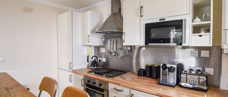 A compact kitchen with white cabinets, a microwave, a gas stove, and a toaster. There are two chairs and a wooden table.