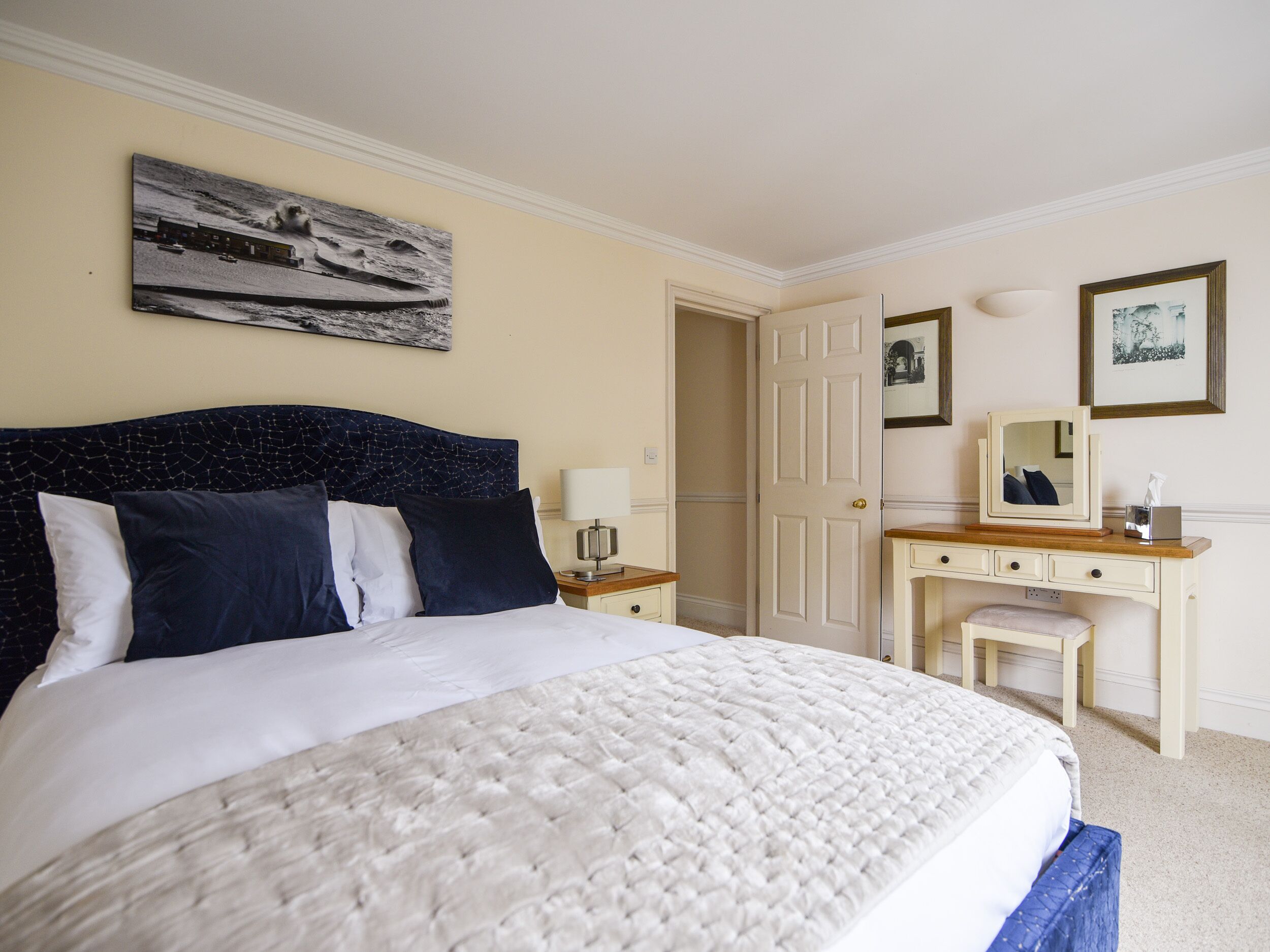 A neatly arranged bedroom with a bed, bedside table, dresser, and a door leading to another room.