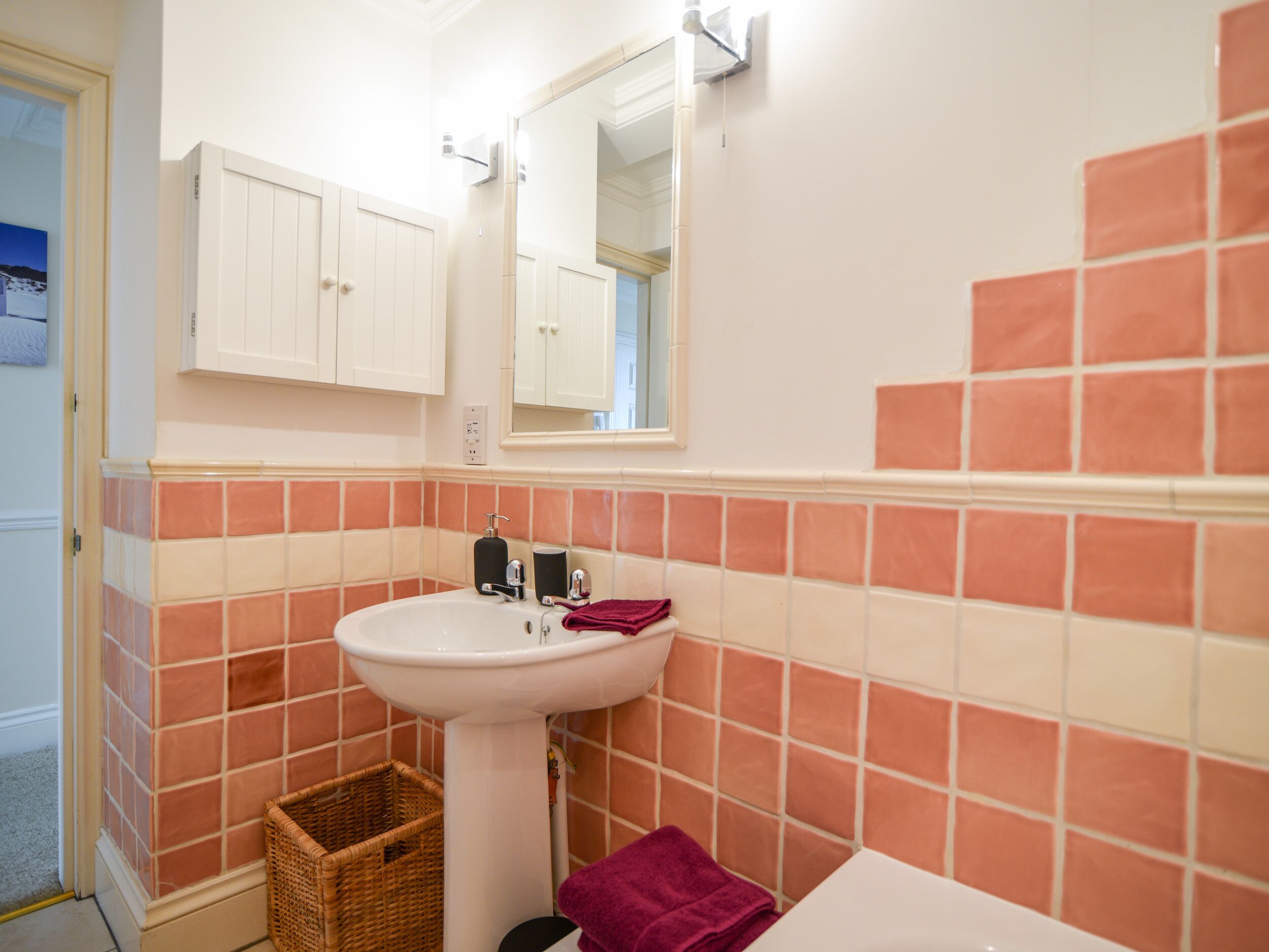 A bathroom with a white sink, a mirror above it, and a tiled wall with a mix of white and orange tiles.