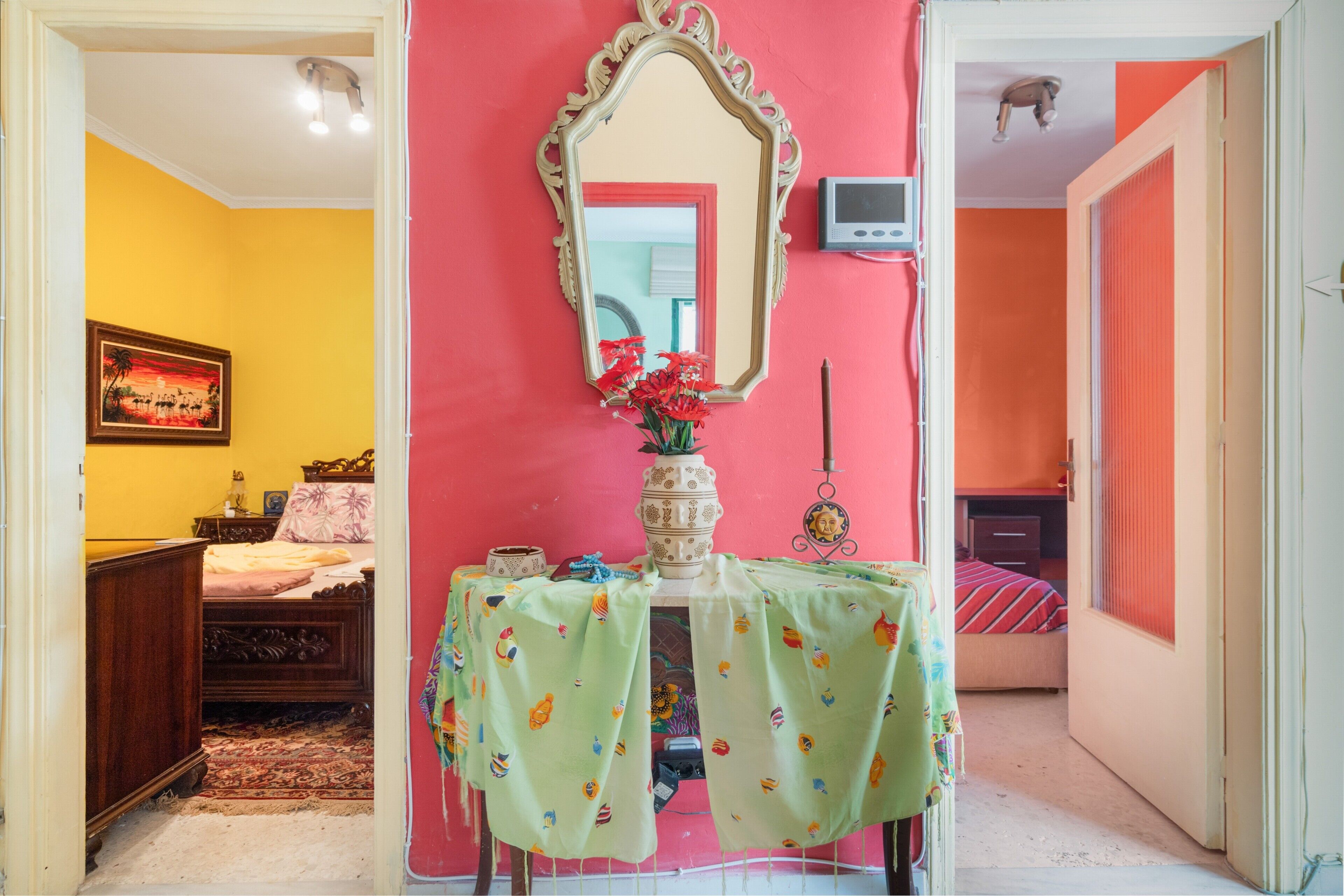 Une chambre avec un lit, une table de chevet ornée d’un vase de fleurs, un miroir et un téléviseur fixé au mur.