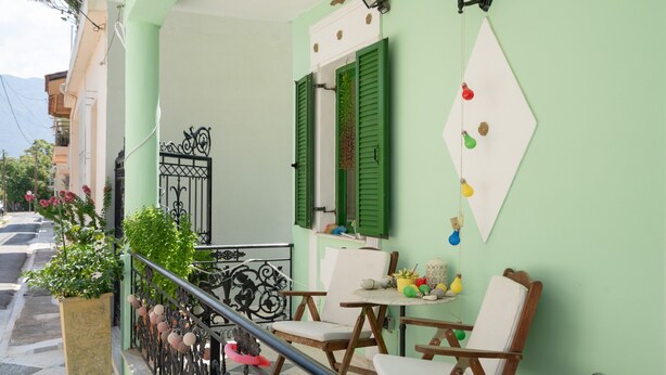 A balcony with a table and chairs, a potted plant, and a decorative wall hanging. - Villa Maria and Dimosthenis with Garden & Wi-Fi (Kalamata)