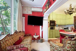 Une pièce comprenant un canapé, un téléviseur, une table à manger et un coin cuisine avec des meubles de couleur verte.
