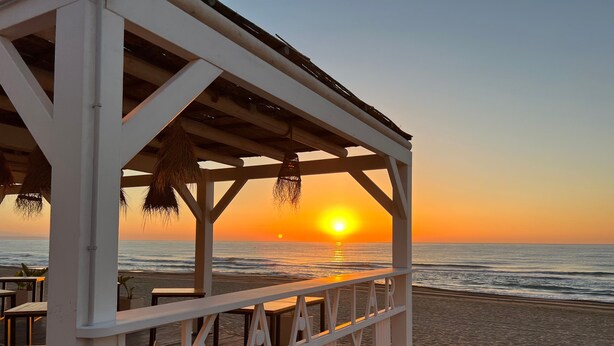 Una construcción frente a la playa con vista al océano y al atardecer.