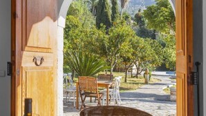 Une porte en bois ouverte donne sur un coin repas où une table est dressée pour deux personnes, avec une bouteille de vin et une assiette de citrons.