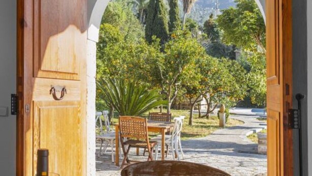 An open wooden door leading to a dining area with a table set for two, a bottle of wine, and a plate of lemons. - Holiday Home "Es Tarongers" with Mountain View, Garden, Terrace & Pool (Sóller)