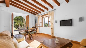 A living room with a wooden ceiling, a TV mounted on the wall, a dining area with a table and chairs, and a sofa. - Holiday Home "Es Tarongers" with Mountain View, Garden, Terrace & Pool (Sóller)